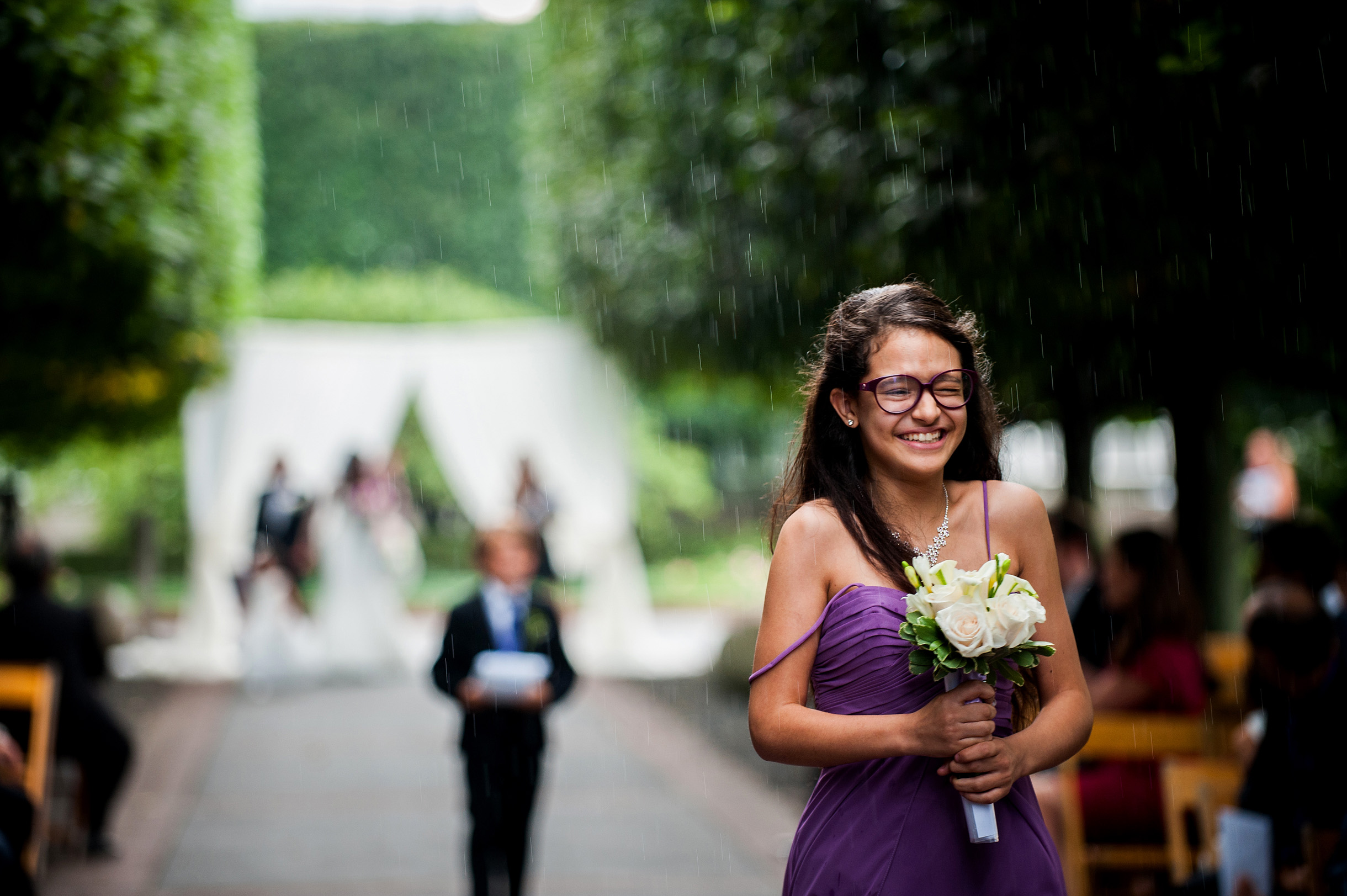 Flowergirl coming down the aisle in rain smiling at the Chicago Botanic Garden