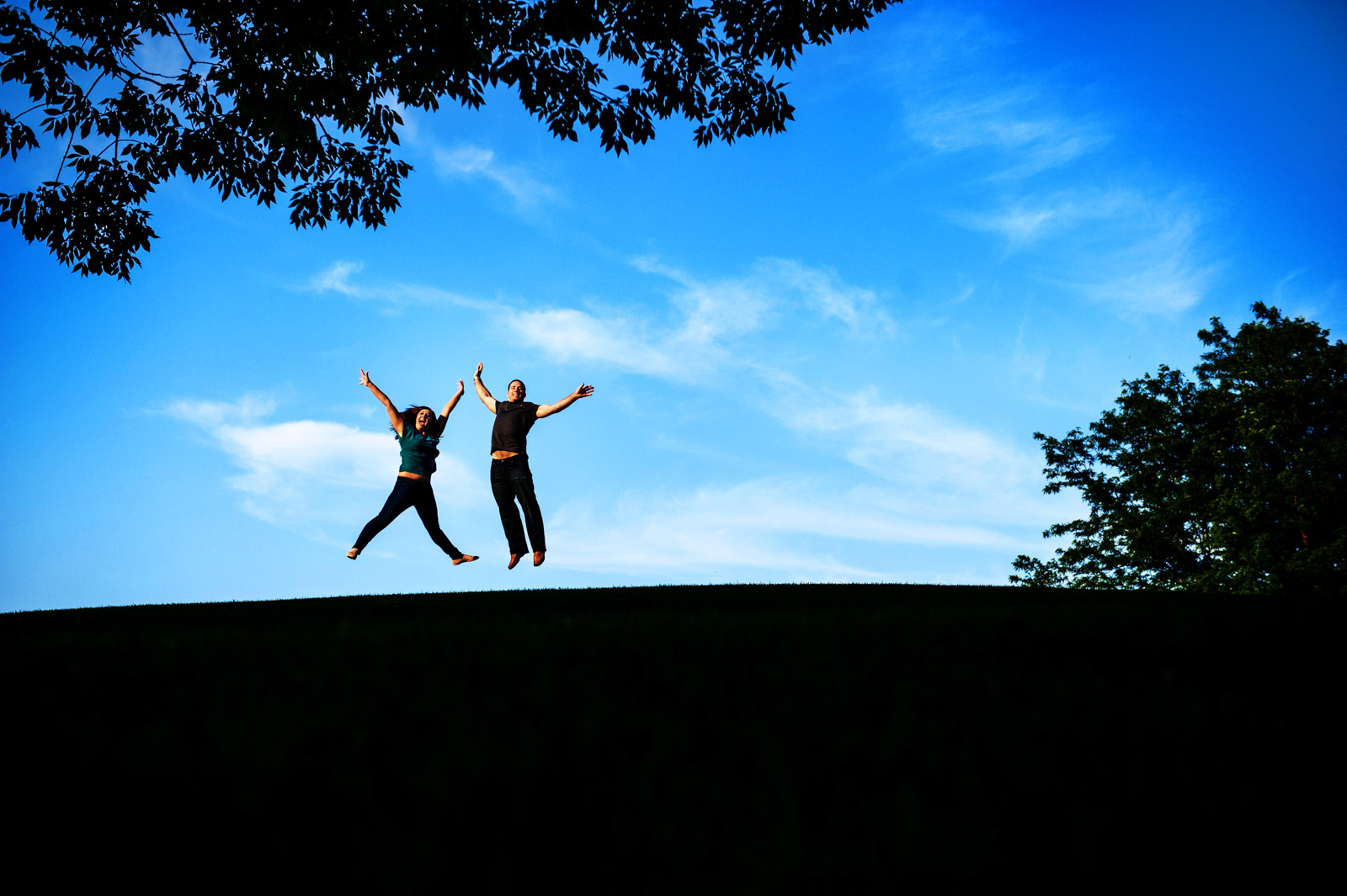 Couple jumping for joy on a hill at sunset during their engagement session