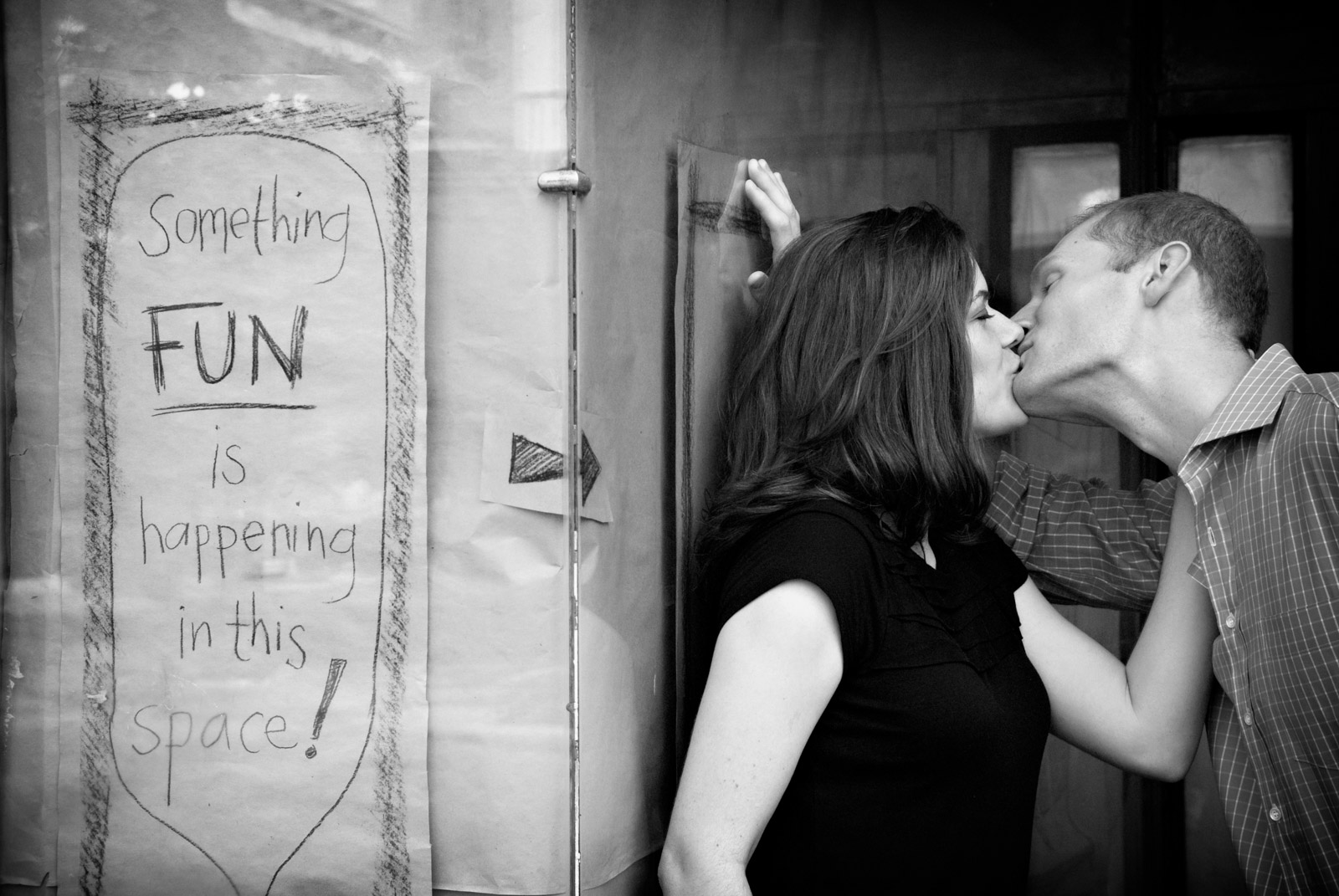Funny engagement session next to sign that reads something fun is happening in this space of rented storefront