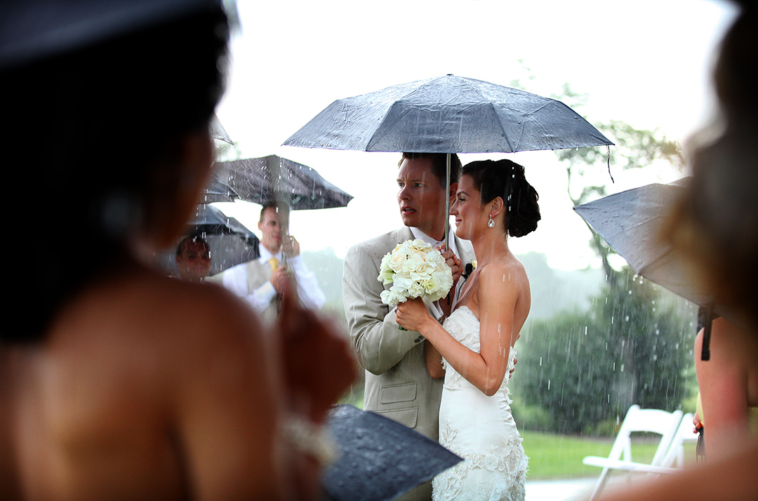 Bride and Groom under umbrella in rain at ceremony 